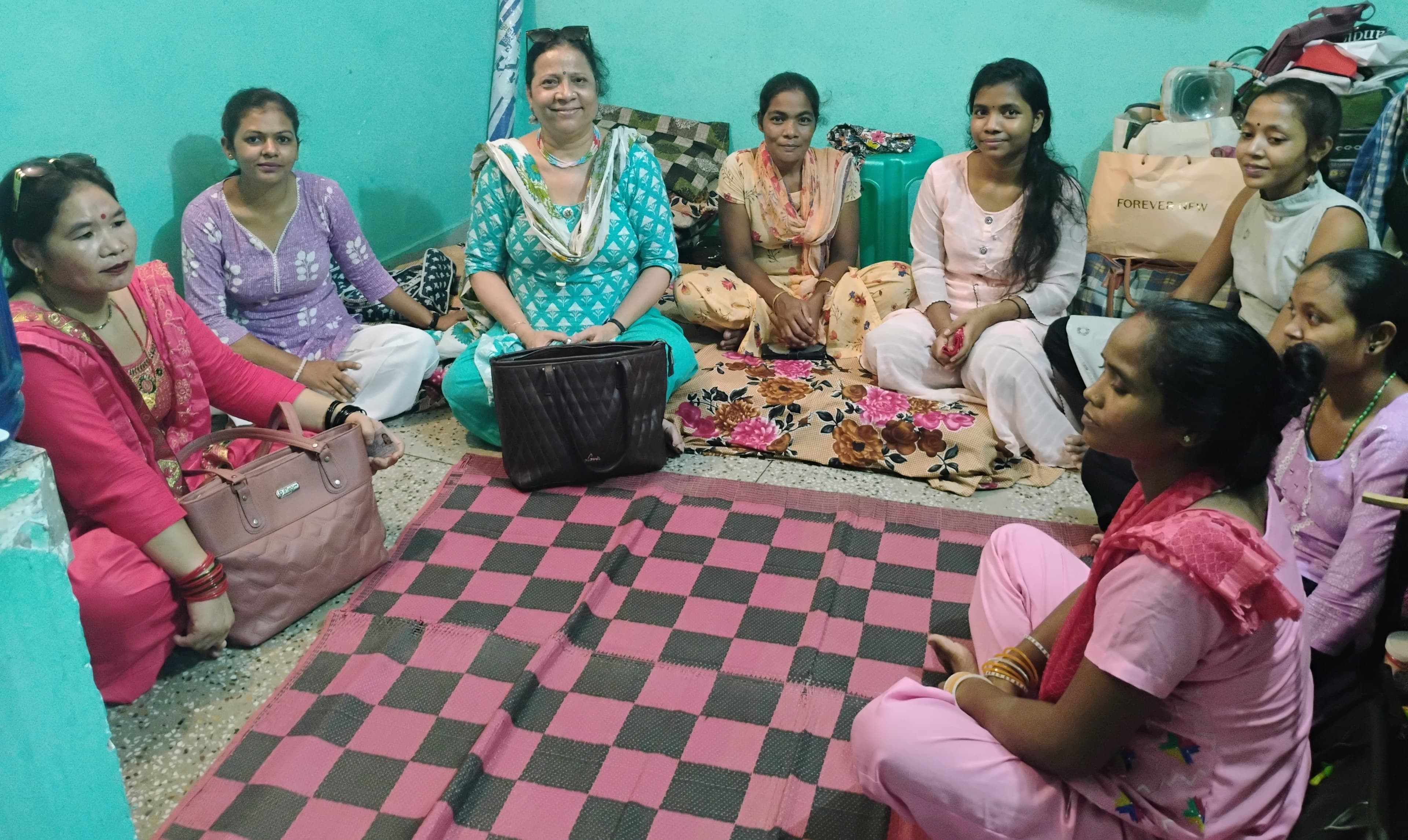A facilitator seated with young girls and women during a group session indoors.