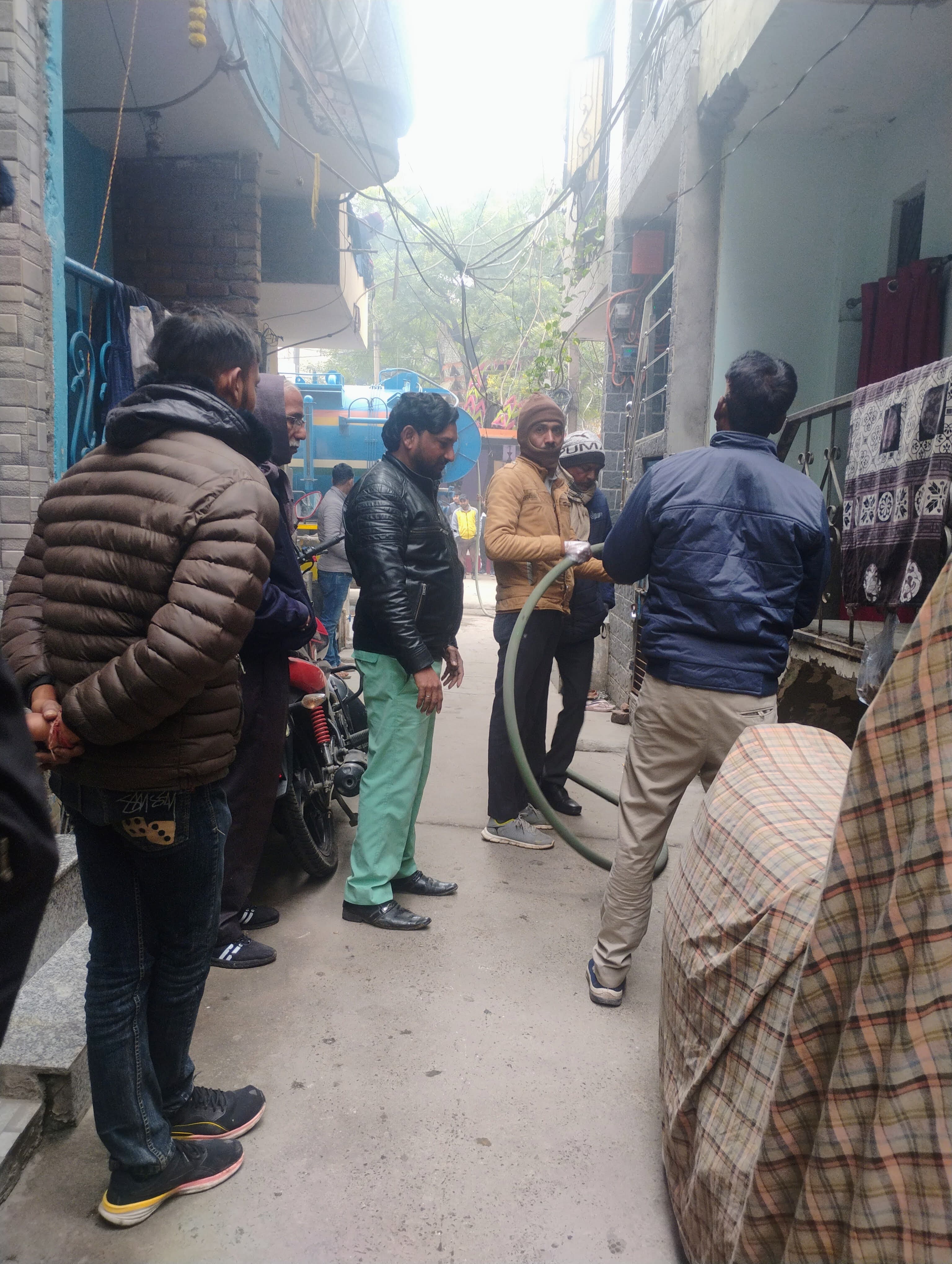 Field activity taking place in a dense Delhi neighborhood lane.
