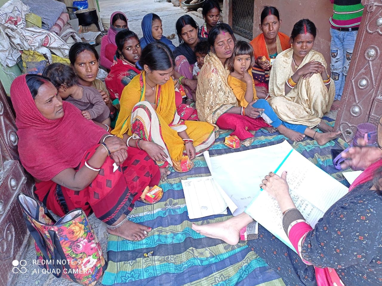 A group of women attending a community meeting and listening to notes being read out.